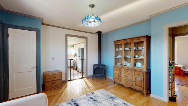 bedroom featuring crown molding, baseboards, light wood-type flooring, freestanding refrigerator, and a wood stove