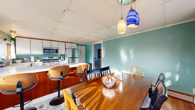 dining area with a baseboard heating unit, a paneled ceiling, and wood finished floors