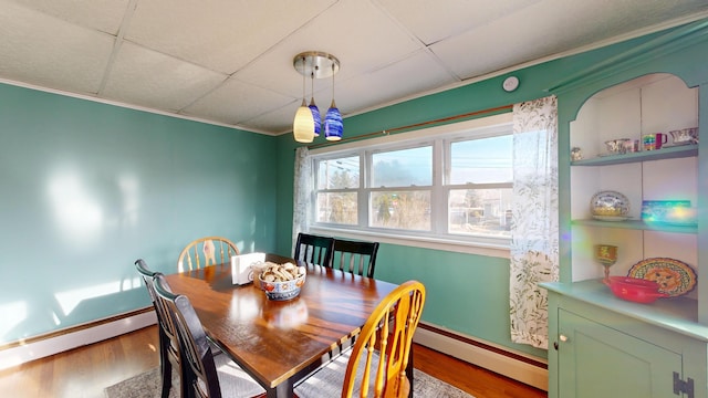 dining space featuring a drop ceiling, a baseboard radiator, wood finished floors, and crown molding