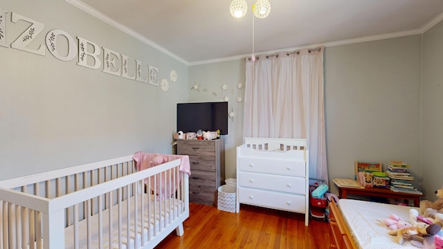 bedroom featuring a nursery area, wood finished floors, and ornamental molding