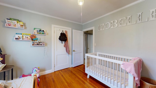 bedroom featuring ornamental molding, a crib, baseboards, and wood finished floors