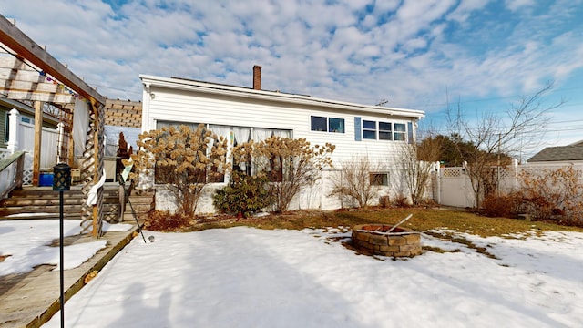 snow covered rear of property featuring a chimney, an outdoor fire pit, and fence