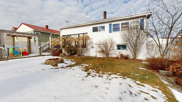 snow covered house with fence, a chimney, and an outdoor fire pit