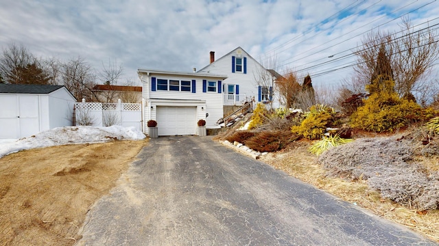 view of front of property with fence, a chimney, a garage, driveway, and a storage unit