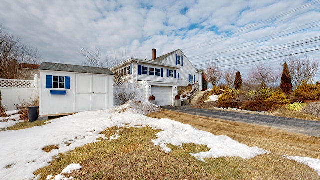 view of front of property featuring aphalt driveway, an attached garage, fence, and a shed