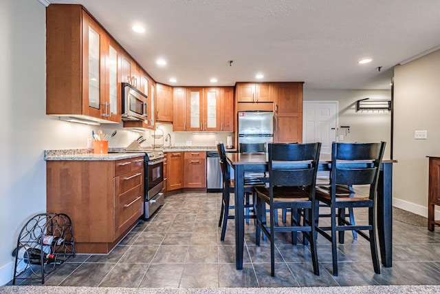 372 Skiway Rd Unit 204, Newry, ME 04261 - kitchen with brown cabinetry, glass insert cabinets, baseboards, appliances with stainless steel finishes, and recessed lighting