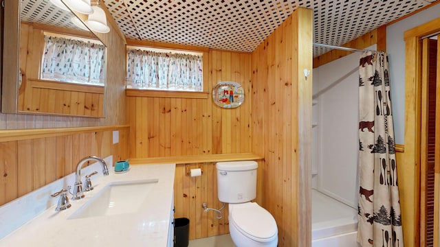 full bathroom with vanity, wood walls, shower / bath combo with shower curtain, and toilet
