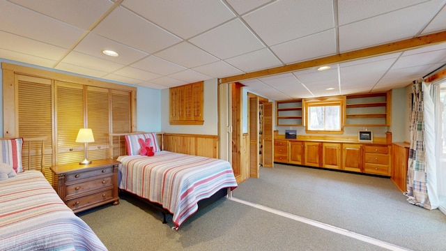 bedroom with a wainscoted wall, light carpet, and a paneled ceiling
