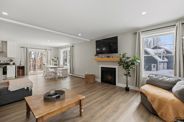 living area featuring beverage cooler, a baseboard radiator, light wood-style flooring, recessed lighting, and a lit fireplace