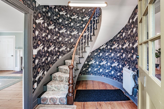 staircase featuring baseboards, radiator, wood finished floors, and wallpapered walls