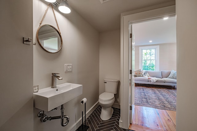 ensuite bathroom with baseboards, toilet, ensuite bathroom, wood finished floors, and a sink