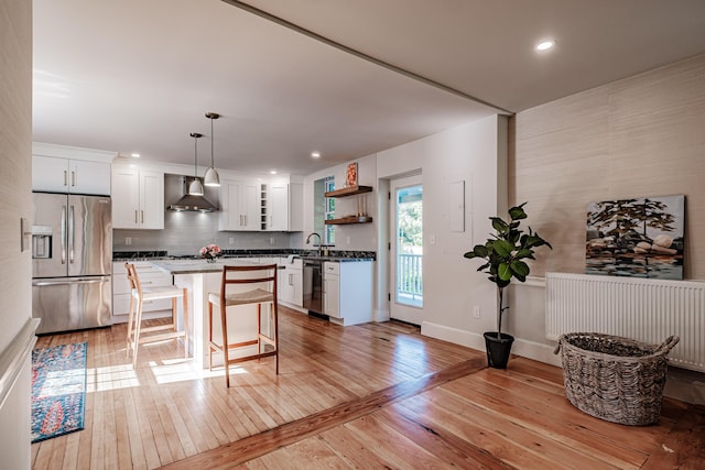 kitchen with a kitchen breakfast bar, wall chimney exhaust hood, light wood-style flooring, and appliances with stainless steel finishes
