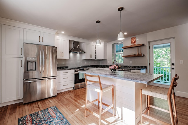 kitchen with open shelves, stainless steel appliances, light wood-style floors, and wall chimney range hood