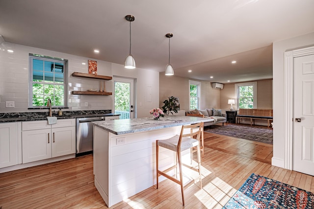 kitchen with light wood-type flooring, backsplash, stainless steel dishwasher, open floor plan, and a wall unit AC