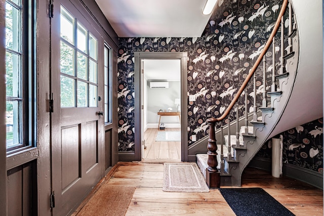 foyer entrance featuring wallpapered walls, a wall unit AC, and wood-type flooring