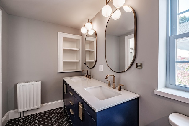 bathroom with double vanity, toilet, radiator heating unit, and a sink