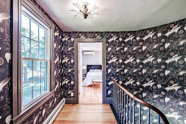 interior space featuring wallpapered walls, baseboard heating, an AC wall unit, and hardwood / wood-style flooring