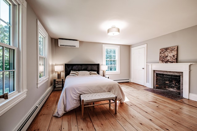 bedroom featuring a fireplace with flush hearth, an AC wall unit, light wood-style flooring, a baseboard heating unit, and a baseboard radiator