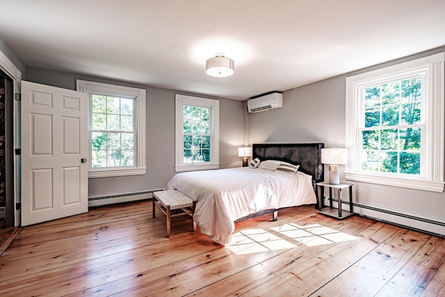 bedroom featuring a baseboard radiator, multiple windows, an AC wall unit, and light wood-style flooring