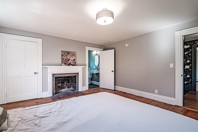 unfurnished bedroom featuring a fireplace with flush hearth, connected bathroom, baseboards, and wood finished floors