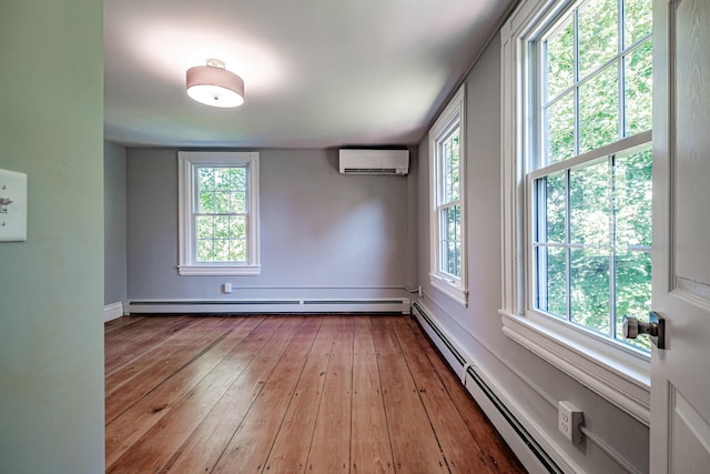 unfurnished room with a wealth of natural light, a baseboard heating unit, an AC wall unit, and hardwood / wood-style flooring