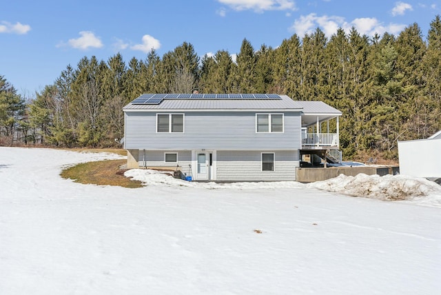 back of property with metal roof, roof mounted solar panels, and a wooded view