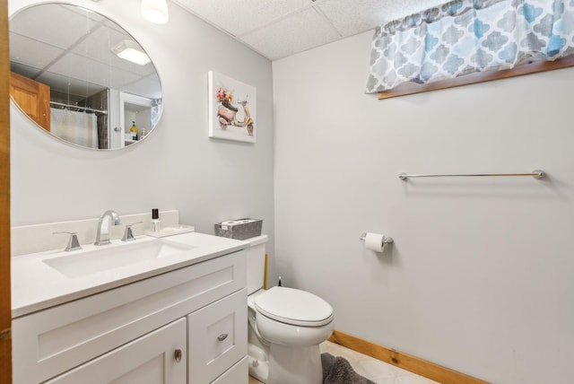 full bathroom featuring curtained shower, baseboards, a drop ceiling, toilet, and vanity