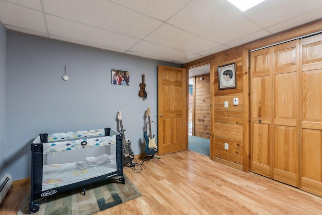 bedroom with a drop ceiling, a baseboard radiator, baseboards, and light wood-style flooring