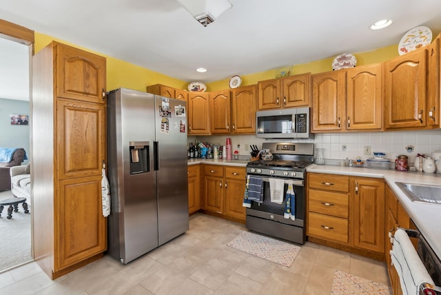 kitchen featuring tasteful backsplash, appliances with stainless steel finishes, light countertops, and brown cabinetry