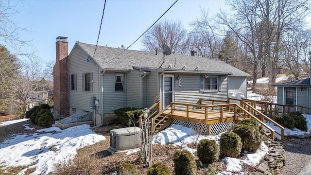 snow covered back of property with a wooden deck, a chimney, and a shingled roof