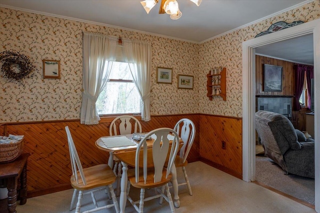 carpeted dining space with wainscoting, wallpapered walls, wood walls, and ornamental molding