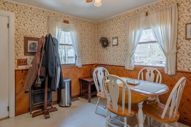 dining space with a wainscoted wall, wooden walls, ornamental molding, and wallpapered walls