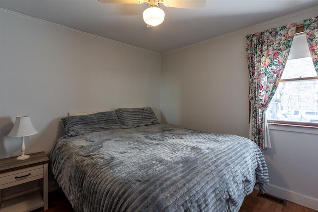 bedroom featuring visible vents, crown molding, baseboards, wood finished floors, and a ceiling fan