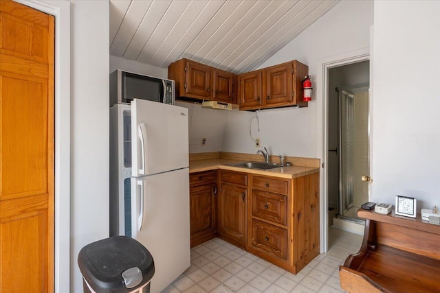 kitchen featuring a sink, stainless steel microwave, freestanding refrigerator, lofted ceiling, and light floors