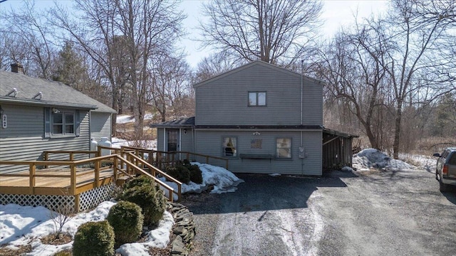 snow covered rear of property featuring a wooden deck and driveway