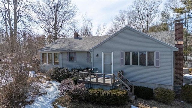 rear view of property with a deck, a chimney, and a shingled roof