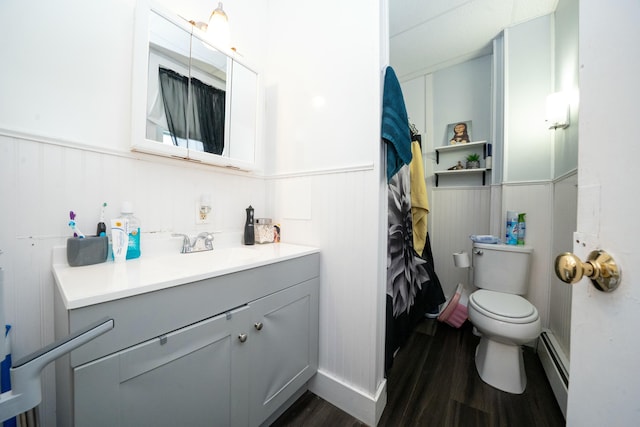 bathroom with vanity, wood finished floors, wainscoting, a baseboard heating unit, and toilet