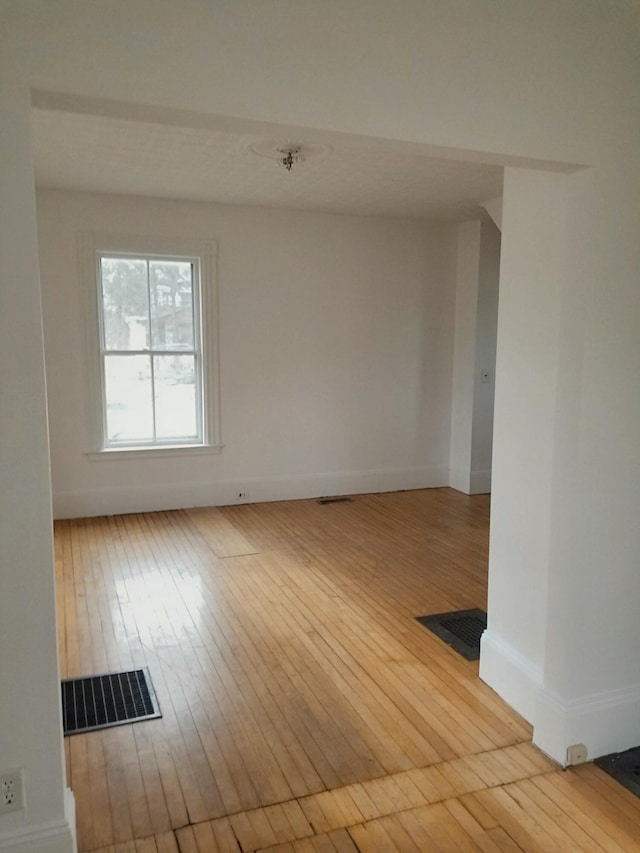 unfurnished room with hardwood / wood-style floors, baseboards, and visible vents