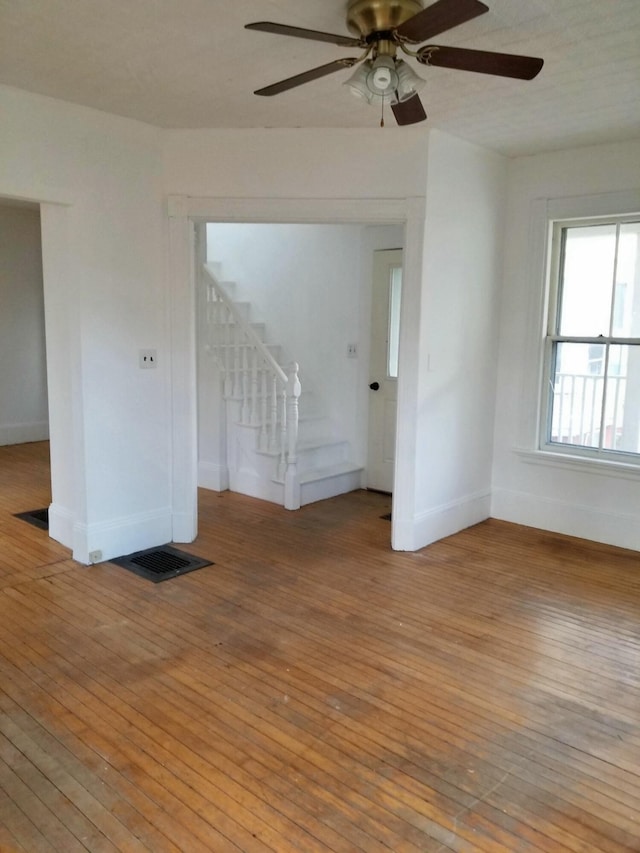 unfurnished room with stairway, baseboards, light wood-style floors, and a ceiling fan