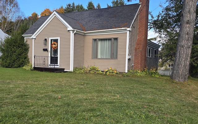 view of front facade featuring a chimney, a front lawn, and a shingled roof