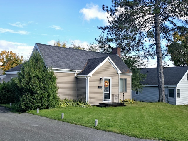 view of front of property with a shingled roof, a front lawn, and a chimney