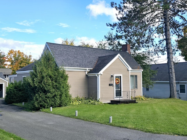 view of front facade with a front yard, roof with shingles, and a chimney