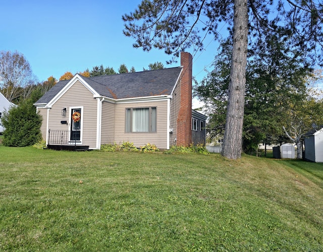 view of front facade featuring a shingled roof, a front yard, and a chimney