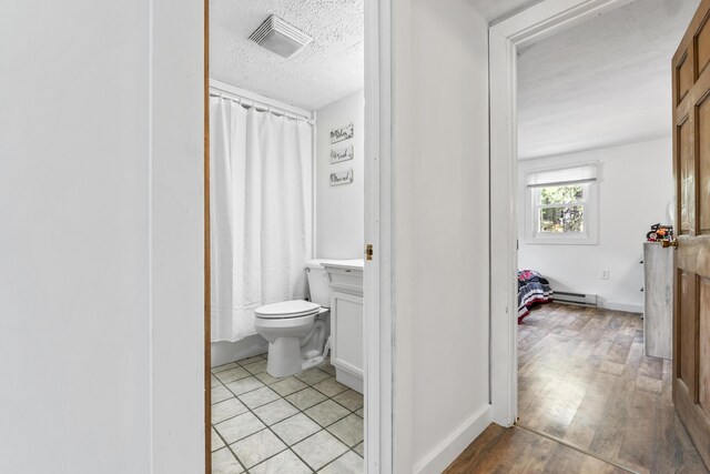 8 Royal Coachman Way, Shapleigh, ME 04076 - bathroom with a baseboard heating unit, a textured ceiling, toilet, wood finished floors, and curtained shower