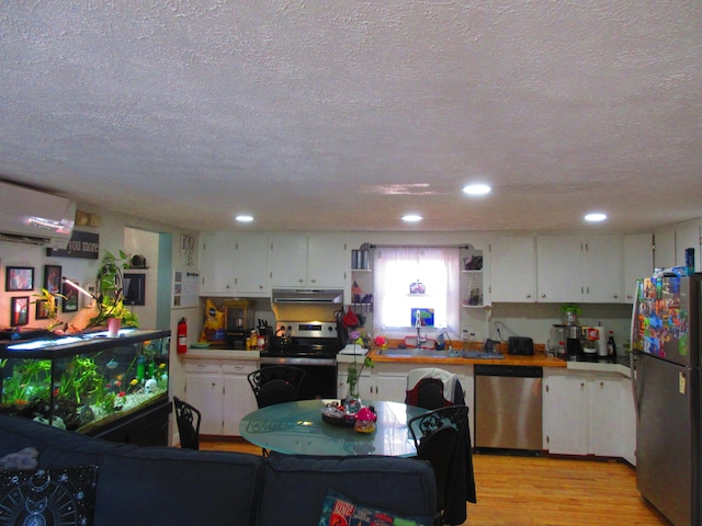 kitchen with a wall mounted AC, under cabinet range hood, open shelves, white cabinetry, and appliances with stainless steel finishes