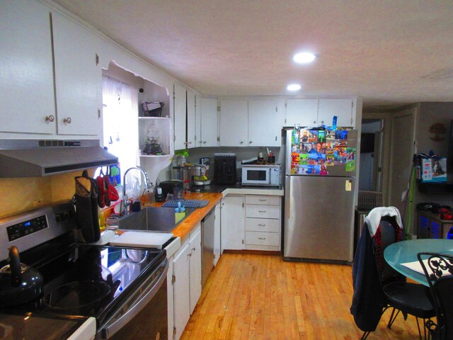 kitchen featuring white cabinetry, under cabinet range hood, appliances with stainless steel finishes, and a sink