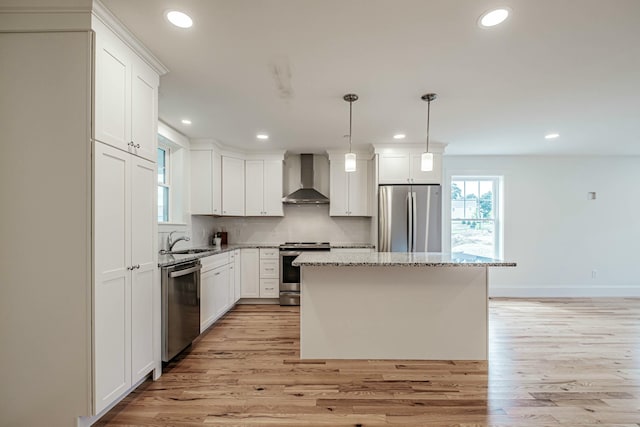 kitchen featuring a sink, stainless steel appliances, wall chimney range hood, light wood-type flooring, and a center island