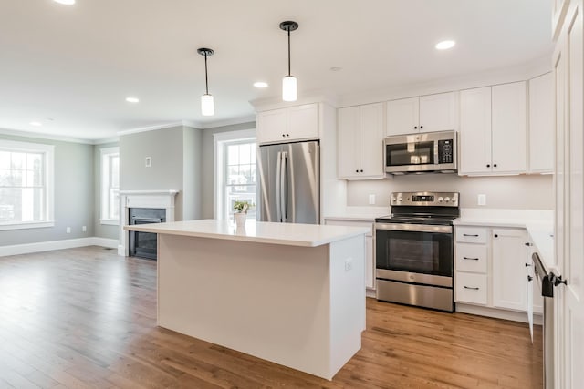 kitchen with stainless steel appliances, a kitchen island, ornamental molding, and light wood-style flooring