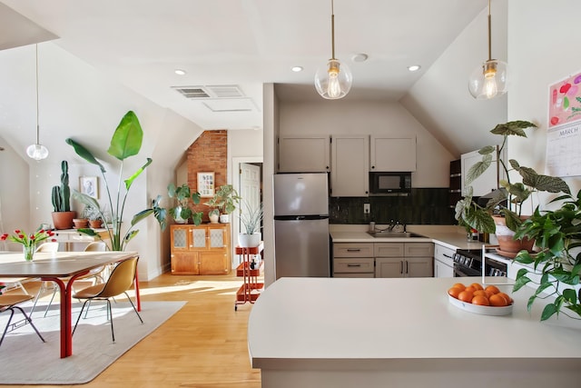 kitchen featuring black microwave, light countertops, lofted ceiling, stainless steel refrigerator, and a sink