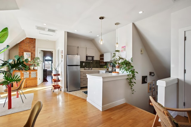 kitchen featuring lofted ceiling, a peninsula, freestanding refrigerator, light countertops, and black microwave